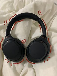 black headphones laying on top of a white sheet with red lines around them and the word love