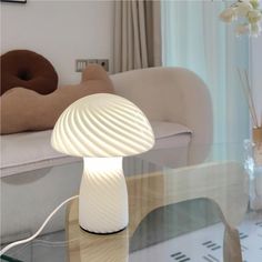 a white lamp sitting on top of a glass table next to a couch in a living room