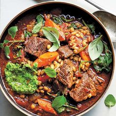 a bowl filled with meat and vegetables on top of a white table next to a spoon