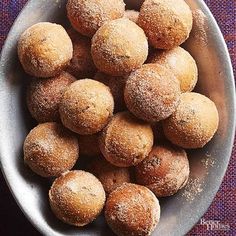 a bowl filled with sugar covered donuts on top of a purple table cloth next to a knife