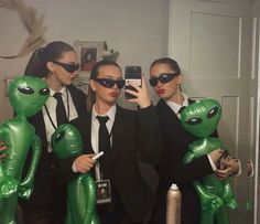 three people in suits and sunglasses are taking a selfie with alien balloons on their heads