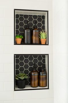 two black shelves with bottles and plants on them in a white tiled bathroom wall mounted above a toilet