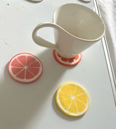 two slices of orange and one slice of grapefruit are on the table next to a white pitcher