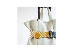 a yellow and white checkerboard bag with a black buckle on it's side