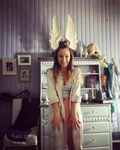 a woman standing in front of a dresser with angel wings on it's head