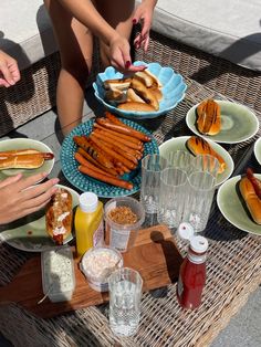 people are sitting at a table with hotdogs and other foods on it,