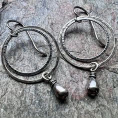 "I have carefully wrapped two sterling silver teardrops in sterling silver wire. The small teardrops dangle below sterling silver circles which I have formed, soldered, and hammered by hand. The earrings hang from handmade sterling silver earwires. Total Earring Length from the top of the ear wire to the bottom of the teardrop is just under 2 inches long. Outer Circle Measures about 1 inch across. Be sure to see all photos and video for size and finish reference. Select your desired finish when Adjustable Teardrop Artisan Hoop Earrings, Sterling Silver Teardrop Hoop Earrings With Polished Finish, Teardrop Sterling Silver Wire Wrapped Hoop Earrings, Hammered Sterling Silver Teardrop Hoop Earrings, Artisan Sterling Silver Nickel-free Teardrop Earrings, Black Pearl Earrings, Silver Chain Earrings, Silver Pearl Earrings, Chalcedony Earrings