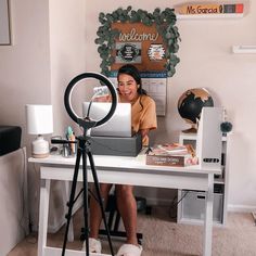 a woman sitting at a desk in front of a laptop on a tripod with a camera next to her