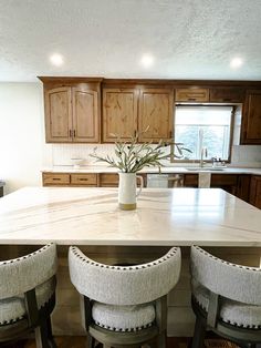 a kitchen island with three stools and a vase on it in the middle of the room