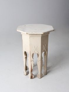 an old white table with carvings on the top and bottom, against a gray background