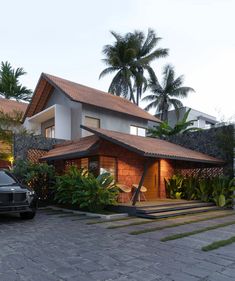 a car parked in front of a house with palm trees and plants around the driveway