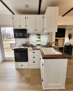 a kitchen with white cabinets, black appliances and wood flooring in the middle of it