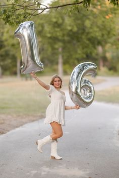 a woman holding two silver balloons in the shape of the letter e and number six