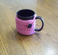 a crocheted coffee cup holder with a black handle on a wooden table top