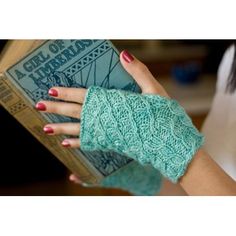 a woman wearing green knitted gloves and holding an old book in her left hand