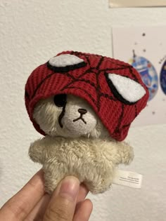 a hand holding a teddy bear wearing a red hat