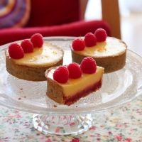 three pieces of cheesecake with raspberry toppings on a glass cake plate