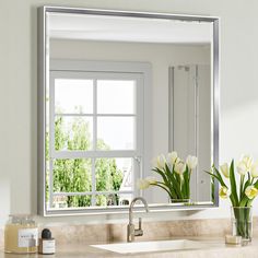 a bathroom sink sitting under a large mirror next to a vase with flowers in it