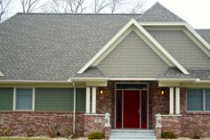 a red door sits in front of a brick house with gray shingles and white trim