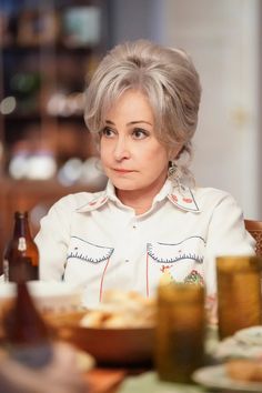 an older woman sitting at a table with food and beer