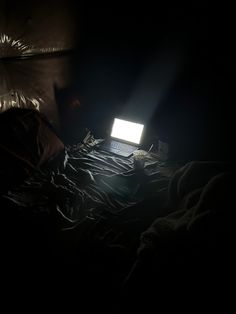 an open laptop computer sitting on top of a bed in the dark under a lamp