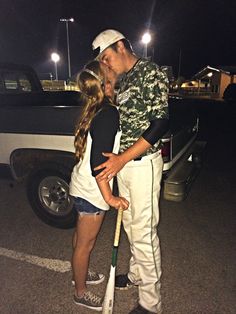 a man and woman kissing while standing next to a baseball bat in the parking lot