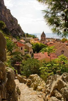 an old town is seen from the top of a hill with trees and rocks in front of it