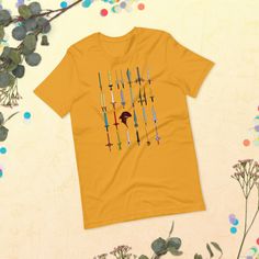 a yellow t - shirt with arrows on it sitting next to some plants and flowers