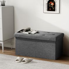 a grey storage bench sitting on top of a wooden floor next to a white dresser