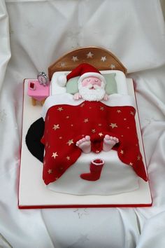 a santa clause sleeping on top of a bed next to a red blanket and pillow