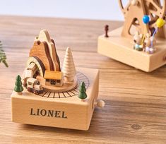 a wooden model of a house with trees on the table next to it and a small tree