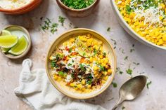 a bowl filled with corn and topped with cheese next to other bowls full of food