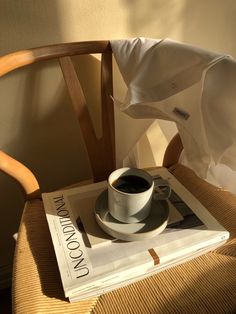 a cup of coffee sitting on top of a white book next to a wooden chair