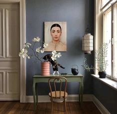 a room with blue walls and a painting on the wall next to a table with flowers in it