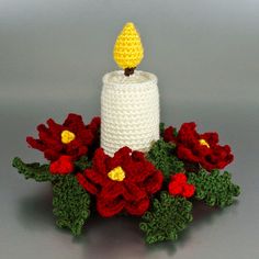 a white crocheted candle surrounded by red and yellow flowers on a gray surface