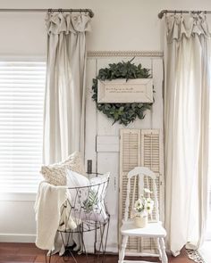 a white chair sitting in front of a window next to a wall with a wreath on it