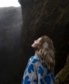 a woman standing in front of a cliff looking up at the sky with her eyes closed