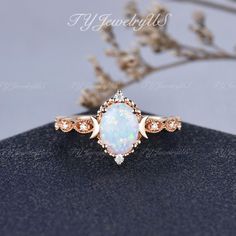 an opal and diamond ring sits on top of a black surface with flowers in the background