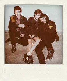 three young people sitting next to each other on the ground in front of a wall