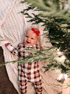 a baby laying on top of a blanket next to a christmas tree with a red bow