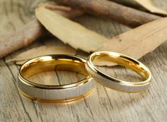 two gold wedding rings sitting on top of a wooden table