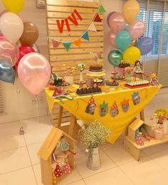 a yellow table topped with lots of balloons and desserts on top of wooden crates