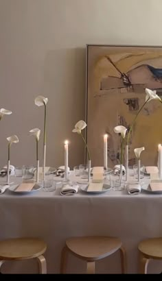 a long table with white flowers and candles on it in front of a large painting