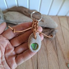 a hand holding a stone with a green tear on it's end and a brown string attached to it