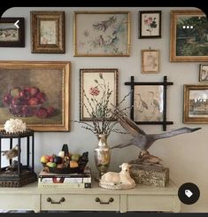 there are many framed pictures on the wall above a dresser with flowers and fruit in vases