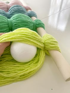 balls of yarn and two skeins of cotton on a white counter top with a rolling pin in the foreground