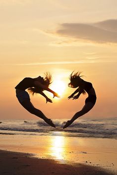 two people jumping into the air with their arms in the shape of a heart at sunset