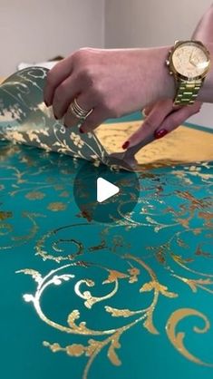 a woman is using a watch on top of a table with gold and green designs