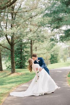 a bride and groom kissing on the road in front of some trees at their wedding