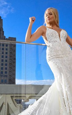 a woman in a white wedding dress posing on a balcony with her arm raised up